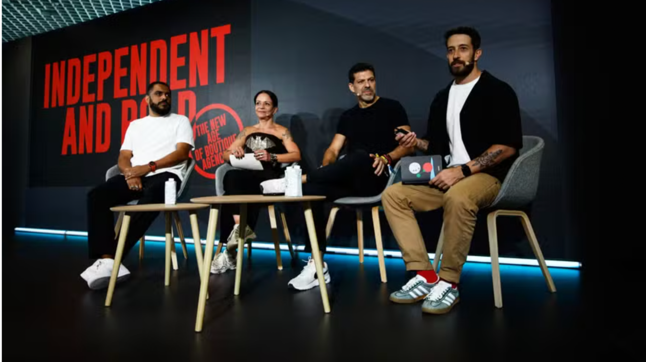 Painel com quatro pessoas sentadas em palco de talk show com letreiro vermelho 'Independent and Bold' ao fundo