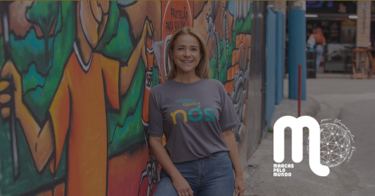Emília Rabello em frente a mural grafitado, usando camiseta da NÓS, com logo "Marcas pelo Mundo" ao lado